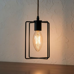 Suspension cage noire géométrique avec une ampoule flamme en verre clair allumée, devant un mur crépi
