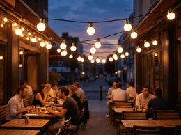 Guirlande d'ampoules globe allumées au-dessus d'une terrasse de restaurant animée, à la tombée de la nuit