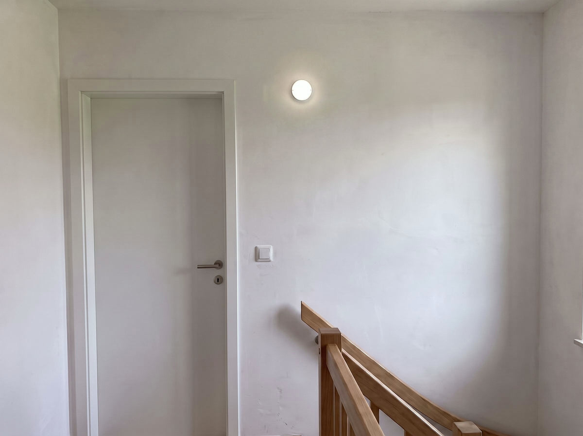 Hublot LED rond à détecteur radar allumé au mur d'un palier d'escalier, lumière blanc neutre