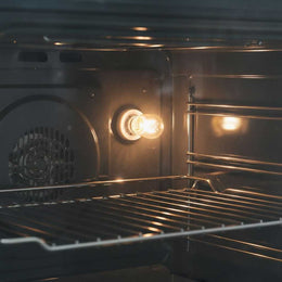Ampoule de four allumée dans la paroi d'un four, éclairant les grilles de cuisson près du ventilateur