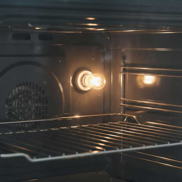 Ampoule de four allumée dans la paroi d'un four, éclairant les grilles de cuisson près du ventilateur