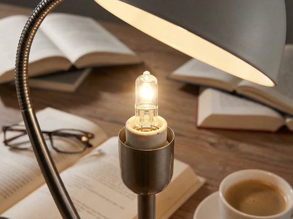 Capsule halogène G9 allumée dans une lampe de bureau en métal, au-dessus de livres ouverts et d'une tasse de café