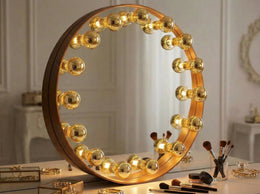 Miroir de maquillage rond bordé d'ampoules sphériques dorées allumées, posé sur une coiffeuse avec pinceaux