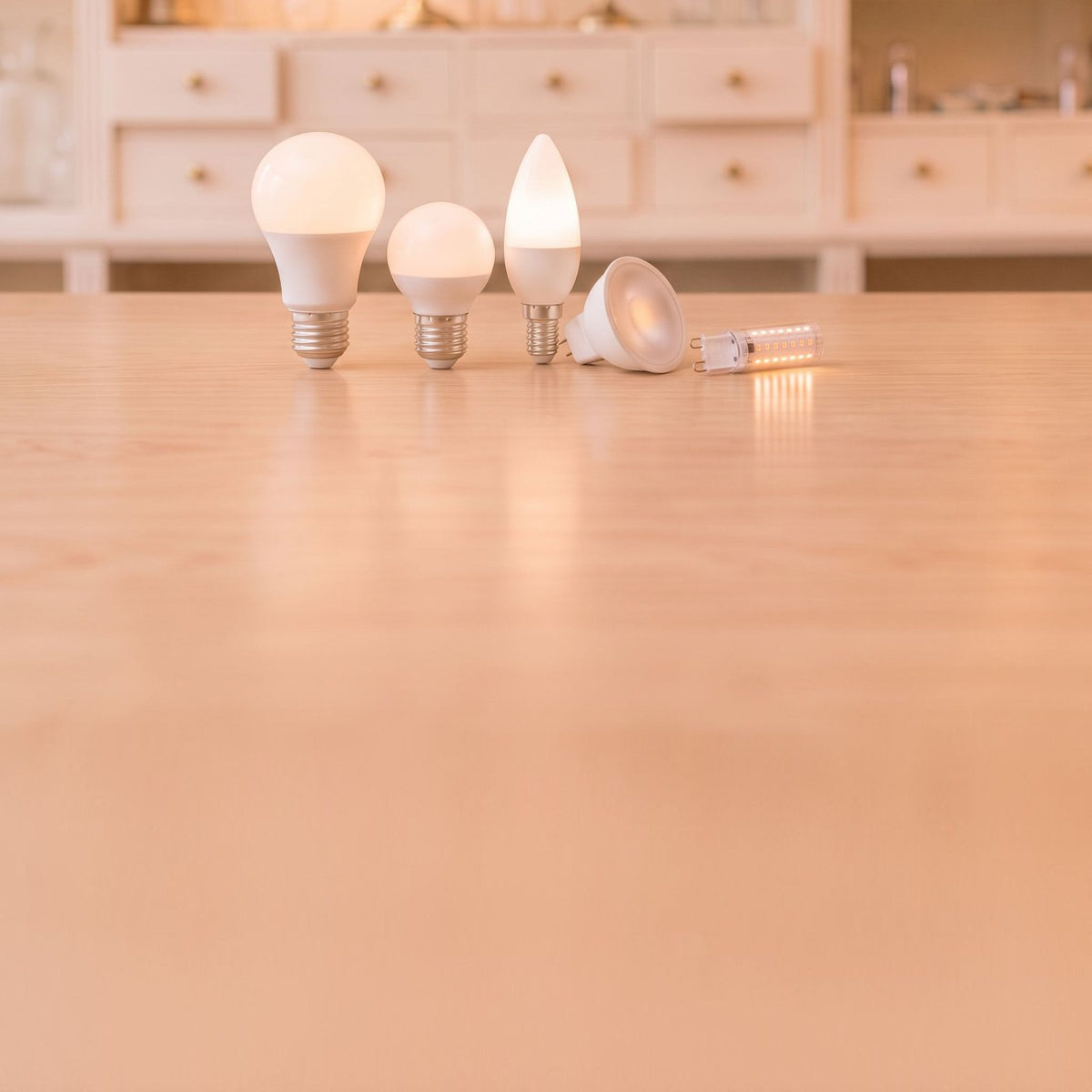 Ampoules LED poire, sphérique et flamme allumées, spot et capsule LED sur un comptoir en bois clair