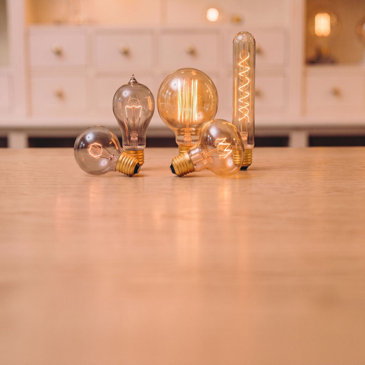 Ampoules vintage à filament apparent allumées, globes, poire et tube en verre ambré sur un comptoir en bois clair