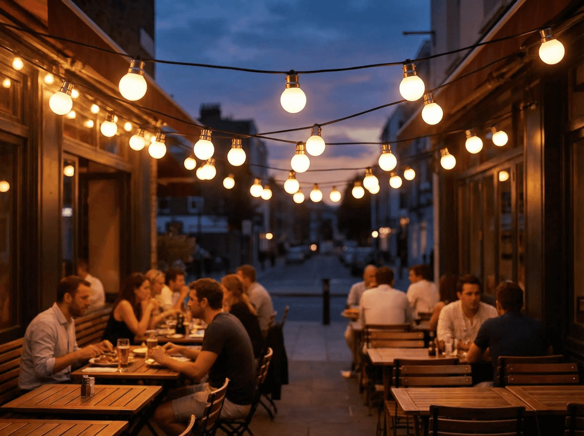 Guirlande d'ampoules globe allumées au-dessus d'une terrasse de restaurant animée, à la tombée de la nuit