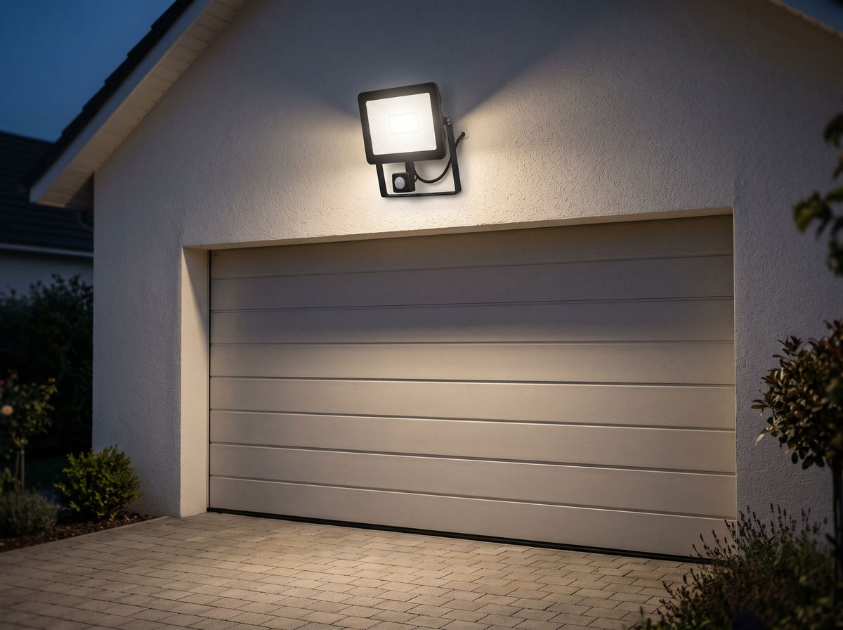 Projecteur LED à détecteur de mouvement fixé sur la façade d'un garage, allumé à la tombée de la nuit