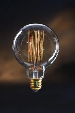 Ampoule globe G95 Swan allumée, filament cage visible et culot E27 en laiton, sur fond sombre