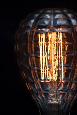Gros plan sur le filament allumé derrière le verre gaufré de l'ampoule Waffle